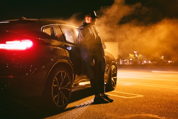 Photo man sitting next to car at night