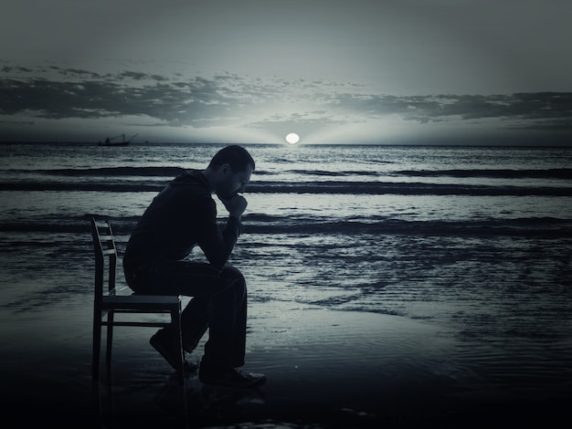 Photo man sitting on the chair on the coast at night