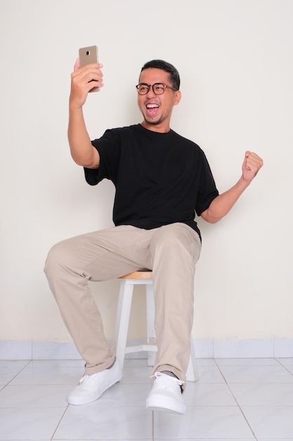 A man sitting on the chair showing excited expression when looking to his phone