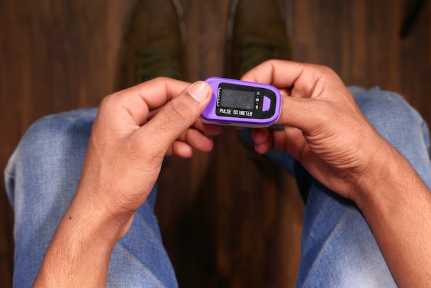 Man sitting on chair using pulse oximeter, top view