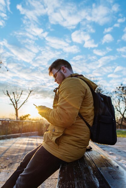 Man sitting in city park with smartphone at sunrise. lifestyle