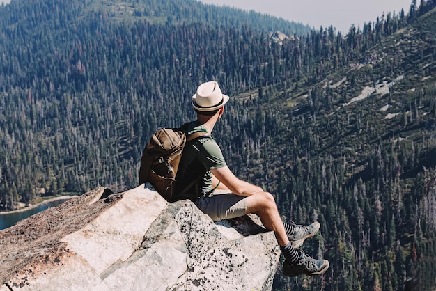 man sitting on the cliff with a beautiful view to mountains backpacking hiking summer activities