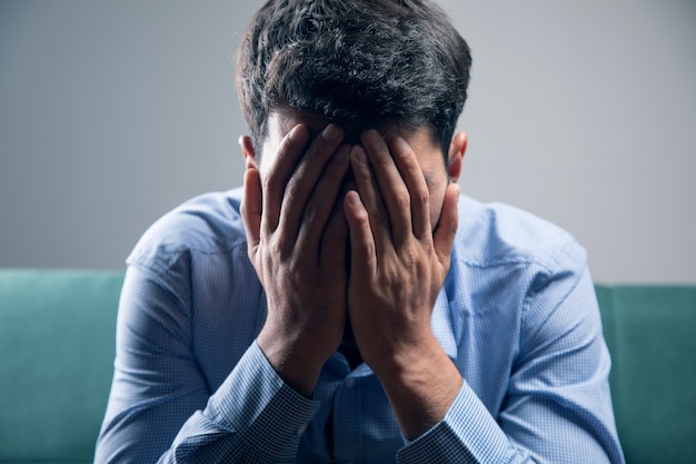 A man sitting on the couch covering his face