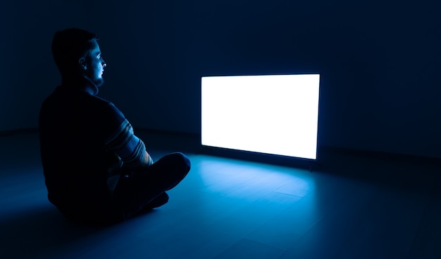 The man sitting in the dark room in front of a white television