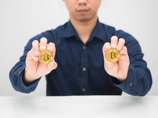 Man sitting at the desk and showing goldden bitcoin in his hand