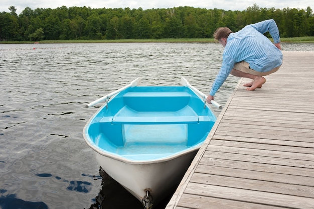 A man sitting on the dock pulls a boat out of the wooden dock with his hand.