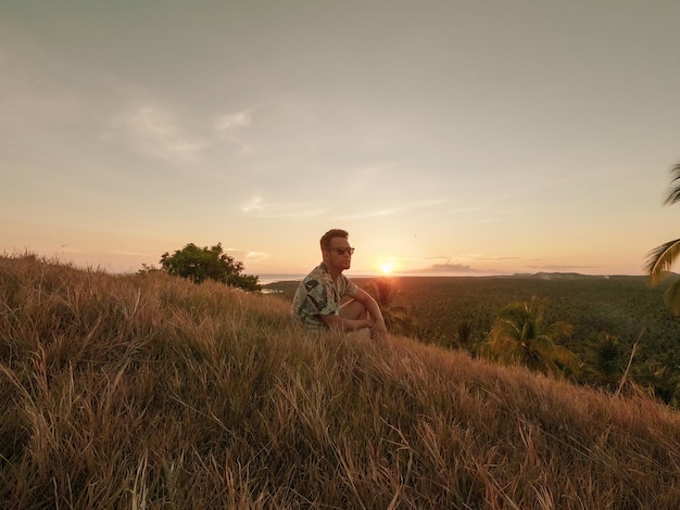 Photo man sitting on field against sky during sunset