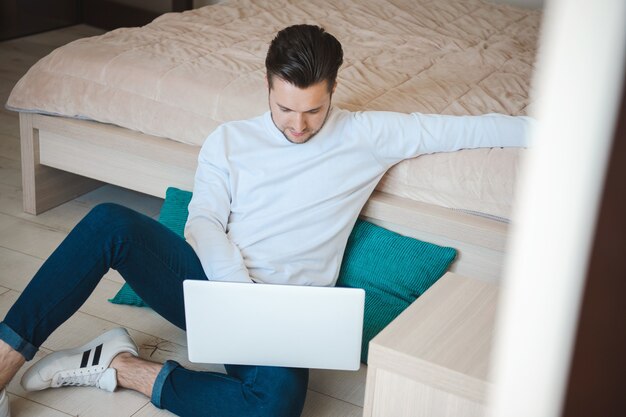 Man sitting on the floor next to the bed working on the computer work atmosphere at home online comm...