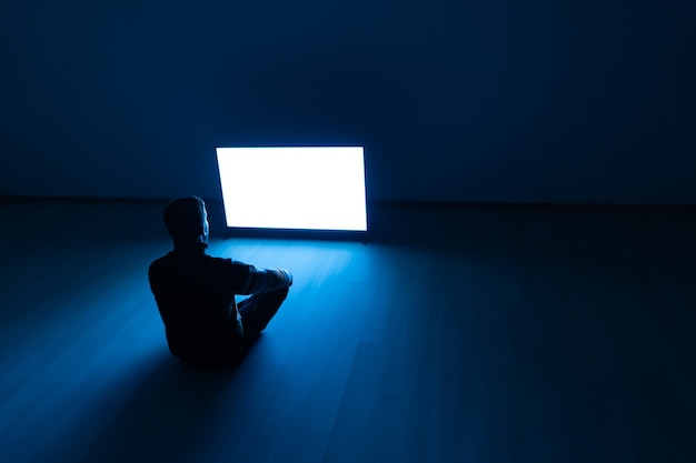 Мужчина сидит на полу перед белым экраном