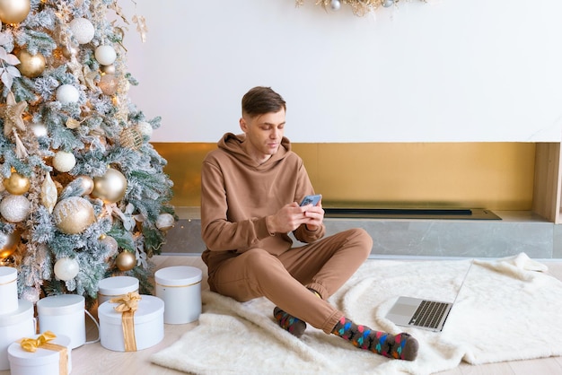 A man sitting on floor near Christmas tree orders online goods on black friday