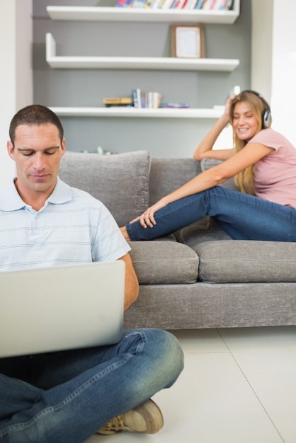 Man sitting on floor using laptop with woman listening to music on the sofa