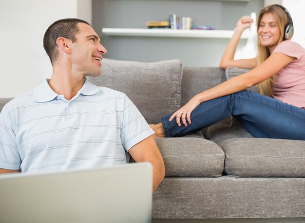 Man sitting on floor with laptop with woman listening to music on the sofa