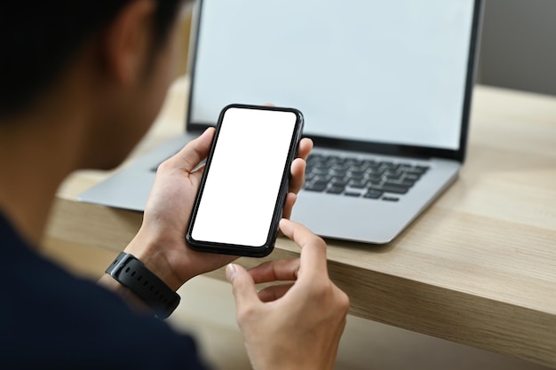 Man sitting front of laptop in living room and using smart phone Over shoulder view