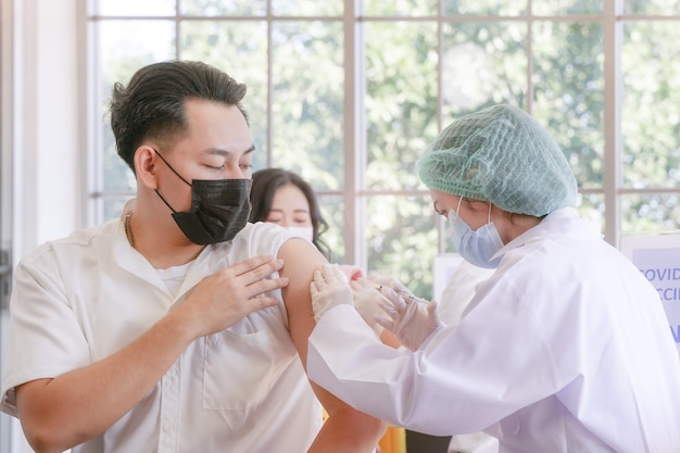 クリニックや病院でワクチンを準備している看護師と一緒にcovidワクチンを接種するために座っている男性