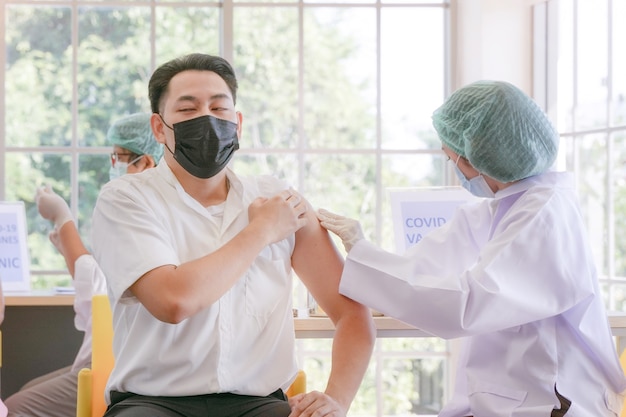 man sitting to getting covid vaccine in clinic or hospital with hand nurse preparing vaccine