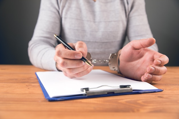 A man sitting in handcuffs signs