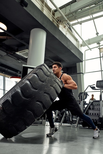 Man sitting on his toes holding a pair of battle ropes for workout guy at the gym working out with fitness rope