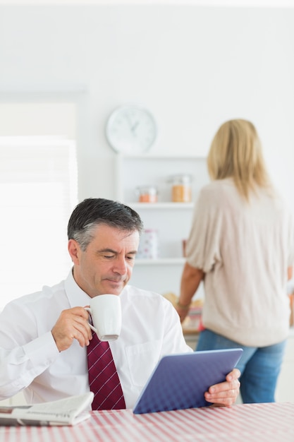 タブレットPCとコーヒーで台所に座っている男