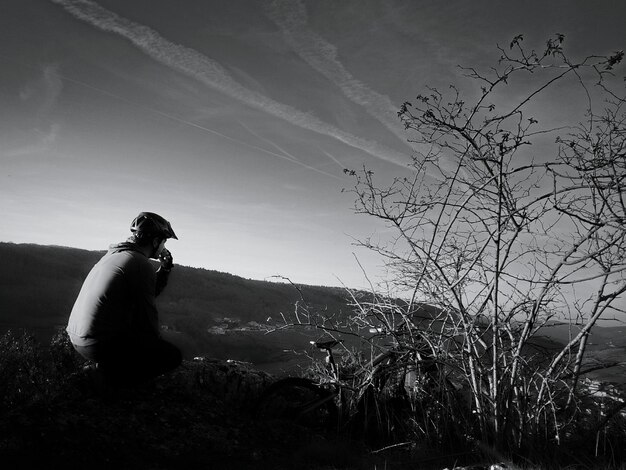 Photo man sitting on landscape against sky