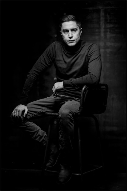 A man sitting on a leather chair on a black background. Card emotions. black and white photo