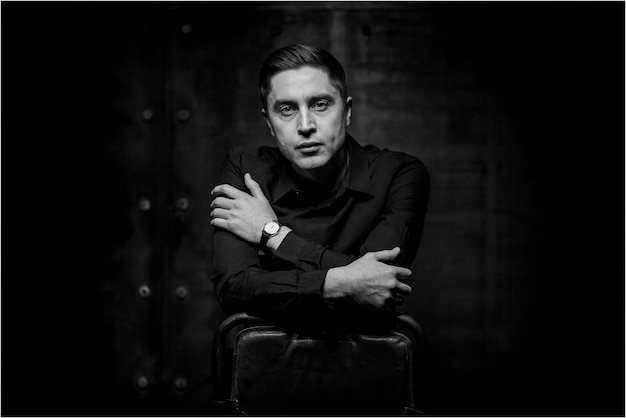 A man sitting on a leather chair on a black background. Card emotions. black and white photo