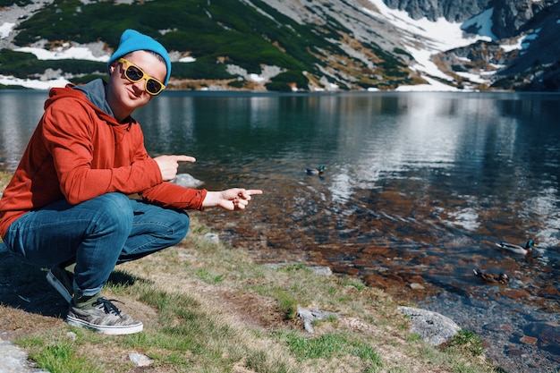 Man sitting near water and pointing on ducks in lake