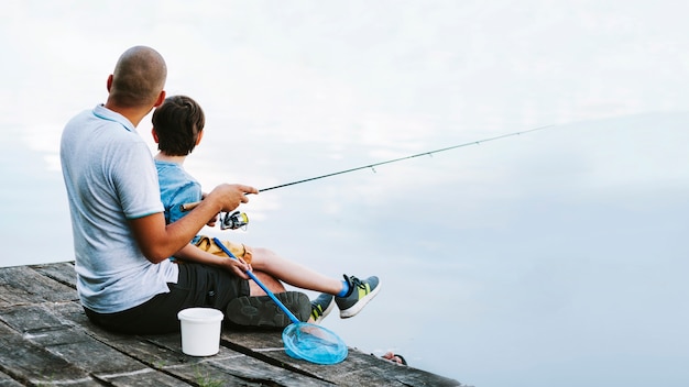 Человек, сидящий на пирсе с сыном, рыбалка на озере