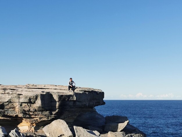 사진 푸른 하늘을 배경으로 바다에 있는 바위 위에 앉아 있는 남자