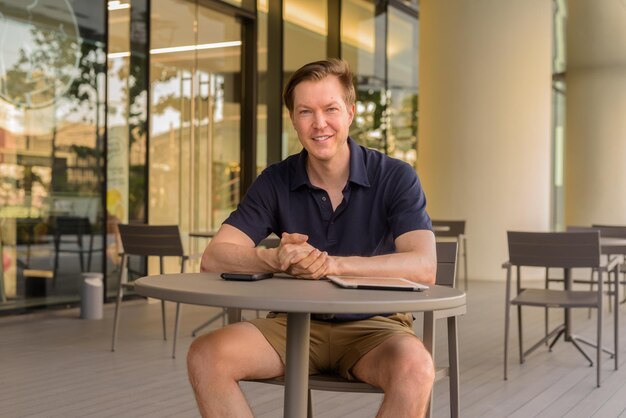 Man sitting outdoors at coffee shop during summer while smiling