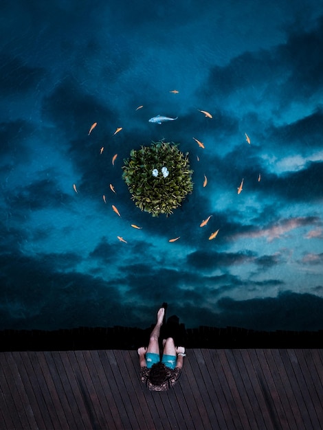 Photo man sitting on pier over sea at night