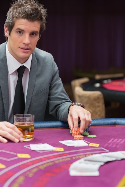 Foto uomo che si siede al tavolo da poker con whisky