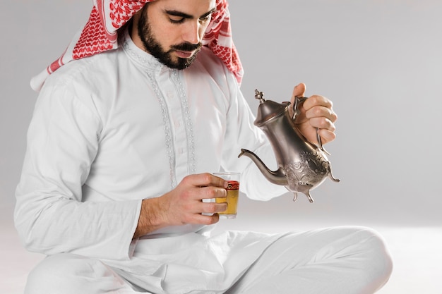 Equipaggi la seduta e il versamento del tè arabo in tazza