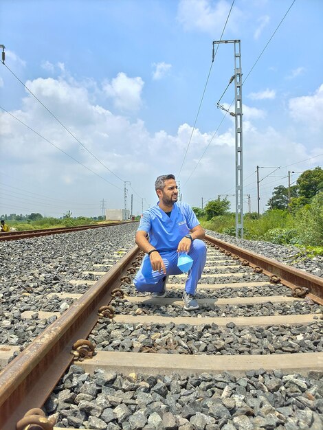 Man sitting on railroad track against sky