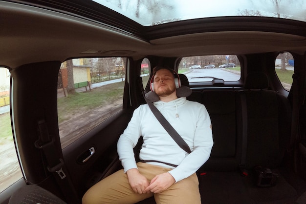 Photo man sitting at the rear sits of the car listening music with headset buckle up with belt copy space