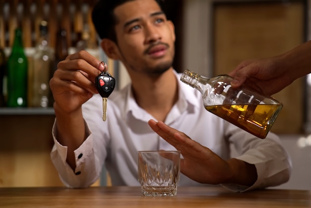 The man sitting in restaurant holding the car key refusing alcohol from his friend.