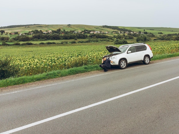 壊れた車の近くの道路に座って助けを求めて車を止めようとしている男