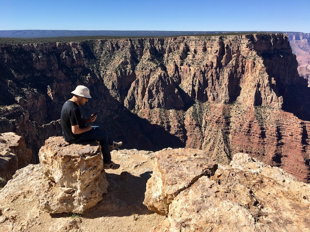 Foto uomo seduto su una roccia contro un cielo limpido