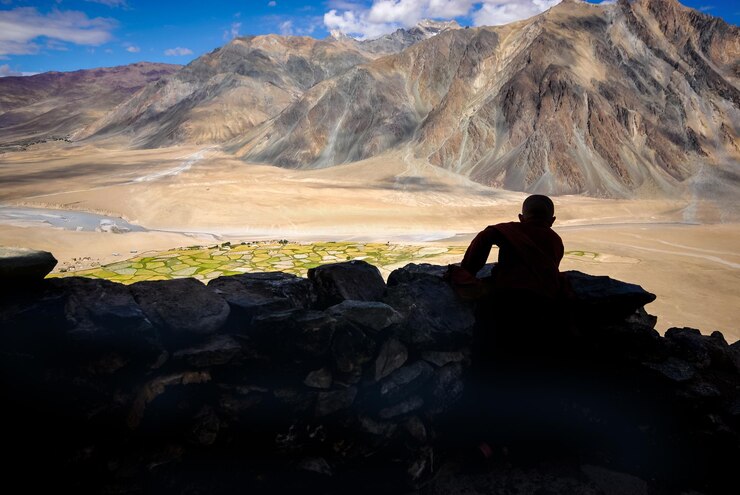 फोटो man sitting on rock by mountains against sky