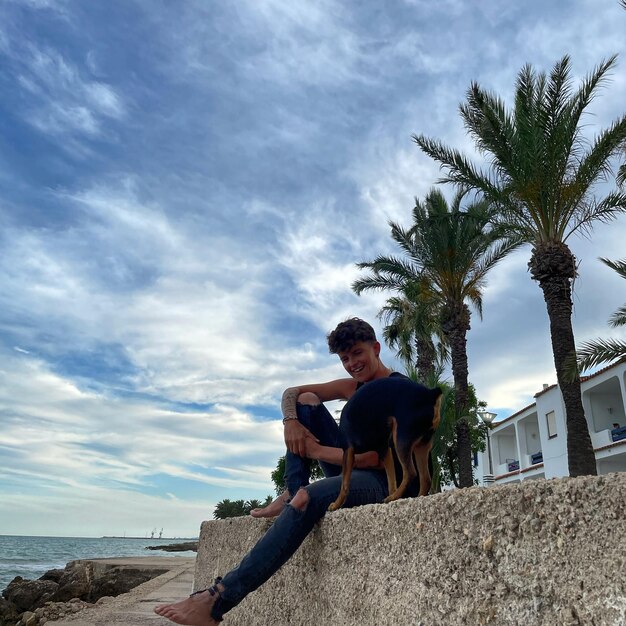 Man sitting on rock by sea against sky