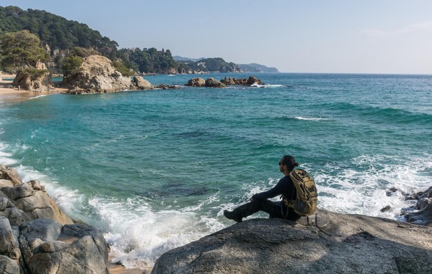 Man sitting on rock by sea against sky