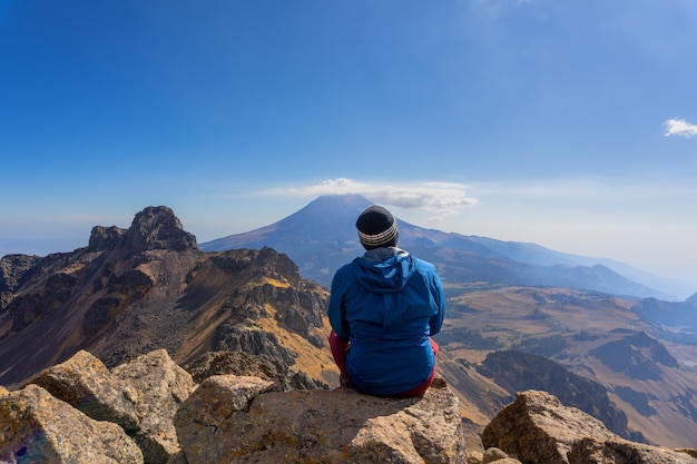 iztaccihuatl 화산의 바위 위에 앉아 있는 남자가 popocatepetl 화산을 관찰합니다.