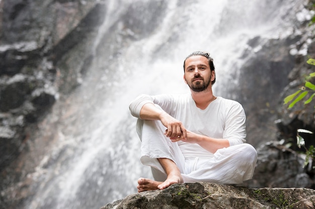 Man sitting on the rock under tropical waterfall