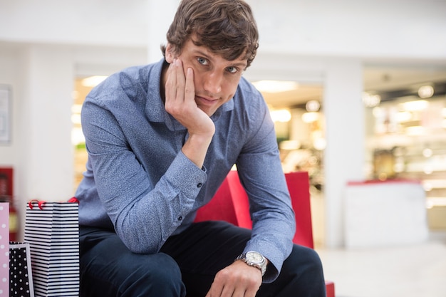 Man sitting in shopping mall with bored expression