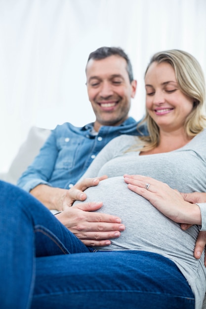 Photo man sitting on sofa and holding pregnant womans stomach