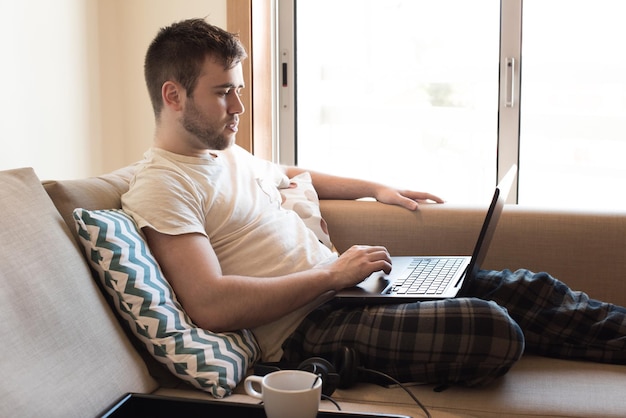 Man sitting on sofa with laptop and a cup of coffee