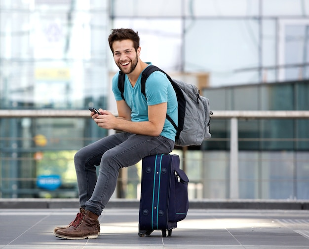 Man sitting on suitcase and sending text message 