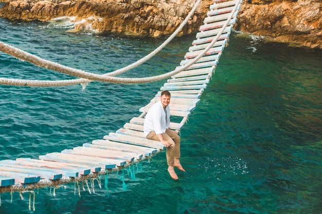 Man sitting at suspension bridge enjoying sea view and nature calmness