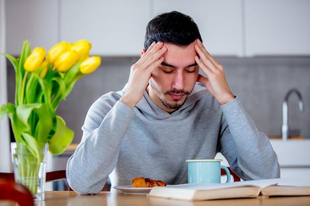 一杯のコーヒーまたは紅茶と本をテーブルに座っている男の人。