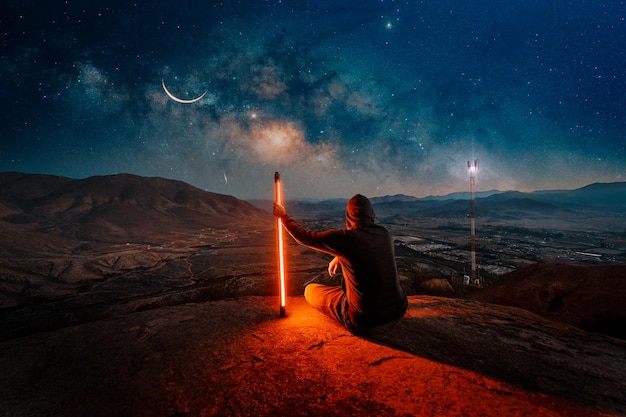 Man sitting on the top of the mountain with led light under the milky way back view