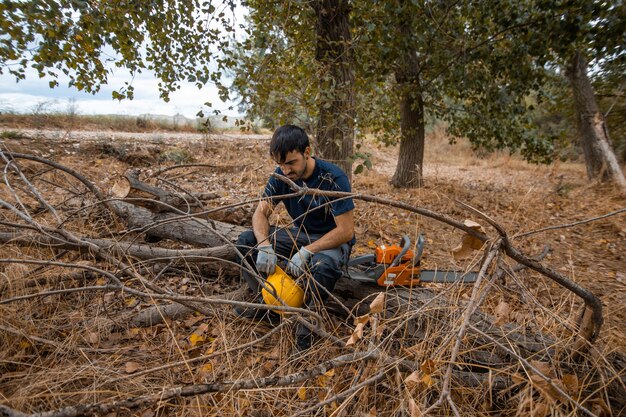 Foto uomo seduto sul tronco di un albero con una motosega nella foresta